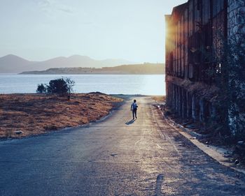 Rear view of man walking on road against sky during sunset