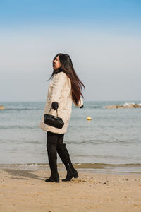 Side view of young beautiful fashion woman standing at beach