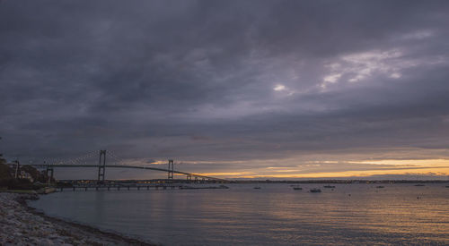 View of suspension bridge over sea against cloudy sky