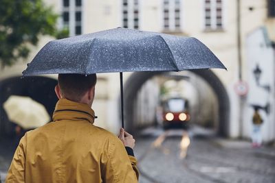 Rear view of man under umbrella during rainy season