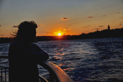 Woman looking at sea against sky during sunset