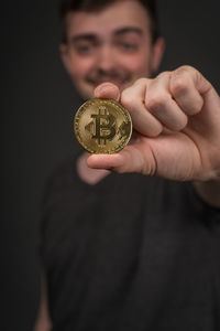 Portrait of young man holding bitcoin against black background
