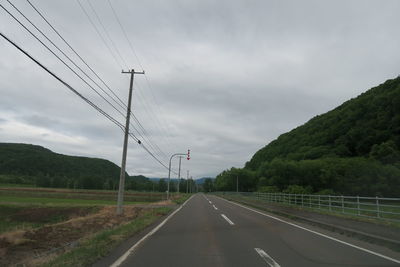 Electricity pylon by road against sky