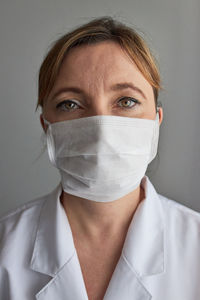Close-up portrait of female doctor wearing mask against gray background