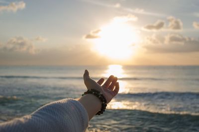 Cropped hand of woman reaching towards sea during sunset