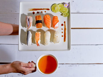 Cropped image of hands holding plate with sushi and drink