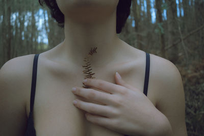 Midsection of woman wearing bra while holding leaf outdoors