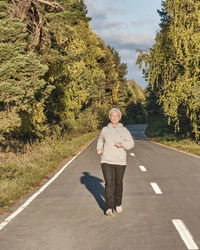 Full length of senior woman running on road in forest 