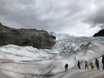 High angle view of people hiking at glaciers against cloudy sky