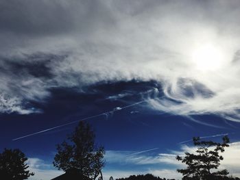 Low angle view of trees against cloudy sky