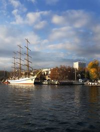 Sailboats in river by buildings against sky