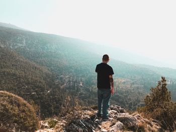 Rear view of man standing on mountain against sky