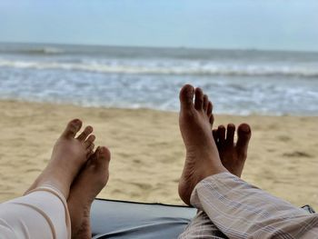 Low section of couple relaxing on lounge chair at beach