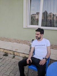 Young man looking down while sitting against window