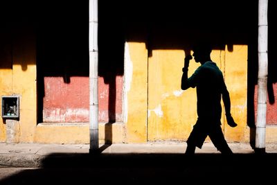 Silhouette man walking on street against colourful building