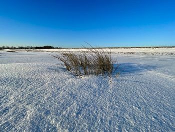 Snow covered land against clear blue sky