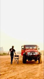 Rear view of man standing on car against sky