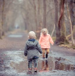 Full length of children walking on puddle in forest