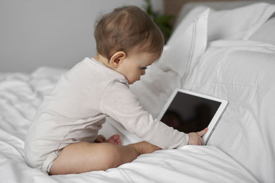Cute girl holding digital tablet sitting on bed