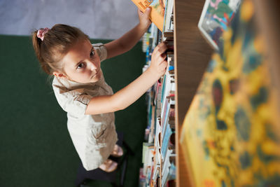 Student looking at top bookshelf in school library. smart girl selecting literature for reading