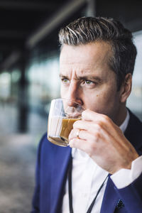 Businessman drinking tea while looking away at workplace