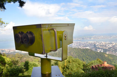 Close-up of metallic coin-operated binoculars over city against sky