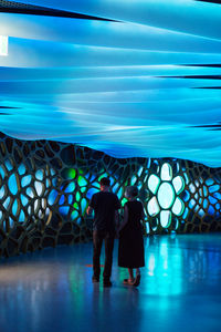 Rear view of couple walking on illuminated lights