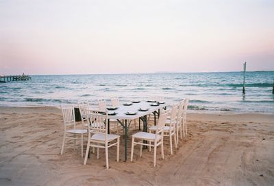 Empty chairs and table on beach against sky