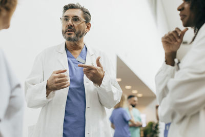 Male physician gesturing while discussing with colleagues at hospital