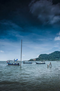 Fishing boats moored in sea against cloudy sky