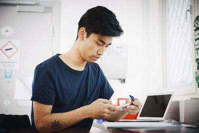 Confident young male university student using smart phone at classroom