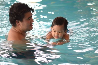 Shirtless father and daughter swimming in pool