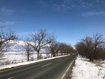 Road amidst bare trees against sky during winter