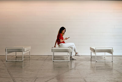 Woman sitting on chair against wall