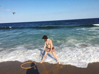 Woman playing on shore at beach against sky