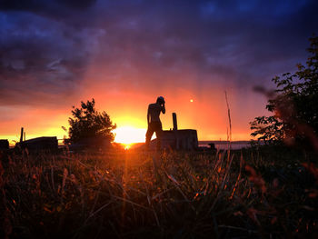 Silhouette man standing on field against sky during sunset