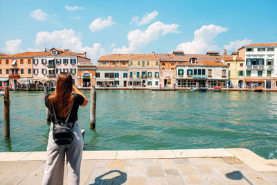 Rear view of woman standing by canal in city