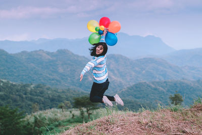 Full length of woman with balloons in mountains against sky