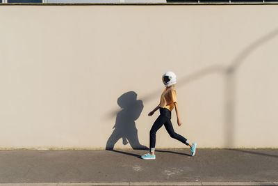 Woman wearing space helmet walking by beige wall