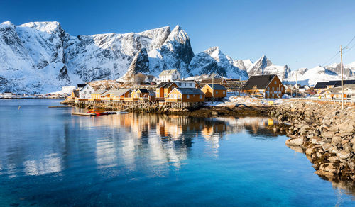 Houses by snowcapped mountains against sky during winter