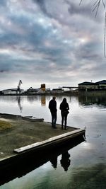 Rear view of silhouette people standing on lake against sky