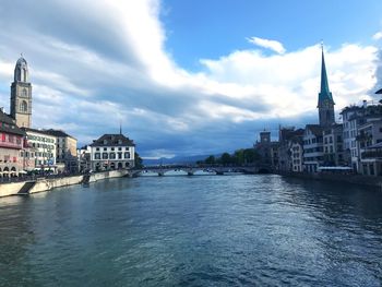 View of buildings by river against sky in city