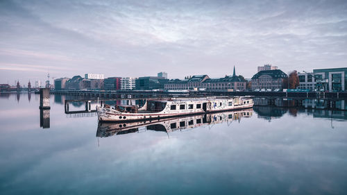 Boat moored on lake by buildings against sky 