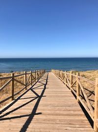 Pier over sea against clear sky on sunny day