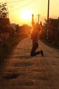 Man jumping on road against sky during sunset