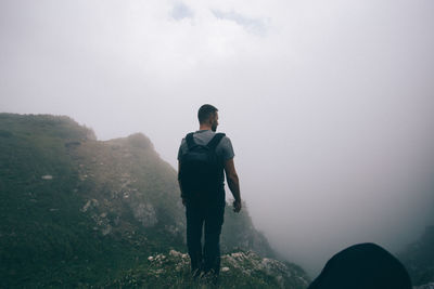 Rear view of man standing on mountain against sky