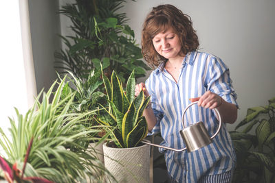 Portrait of young woman standing by potted plant