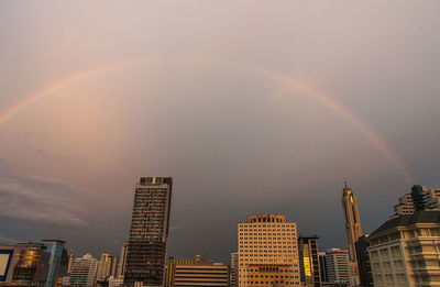 Low angle view of rainbow over buildings in city against sky