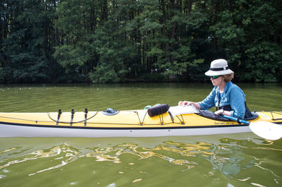 Man sitting in boat on lake against trees