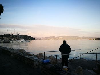 Man standing on shore against sky during sunset